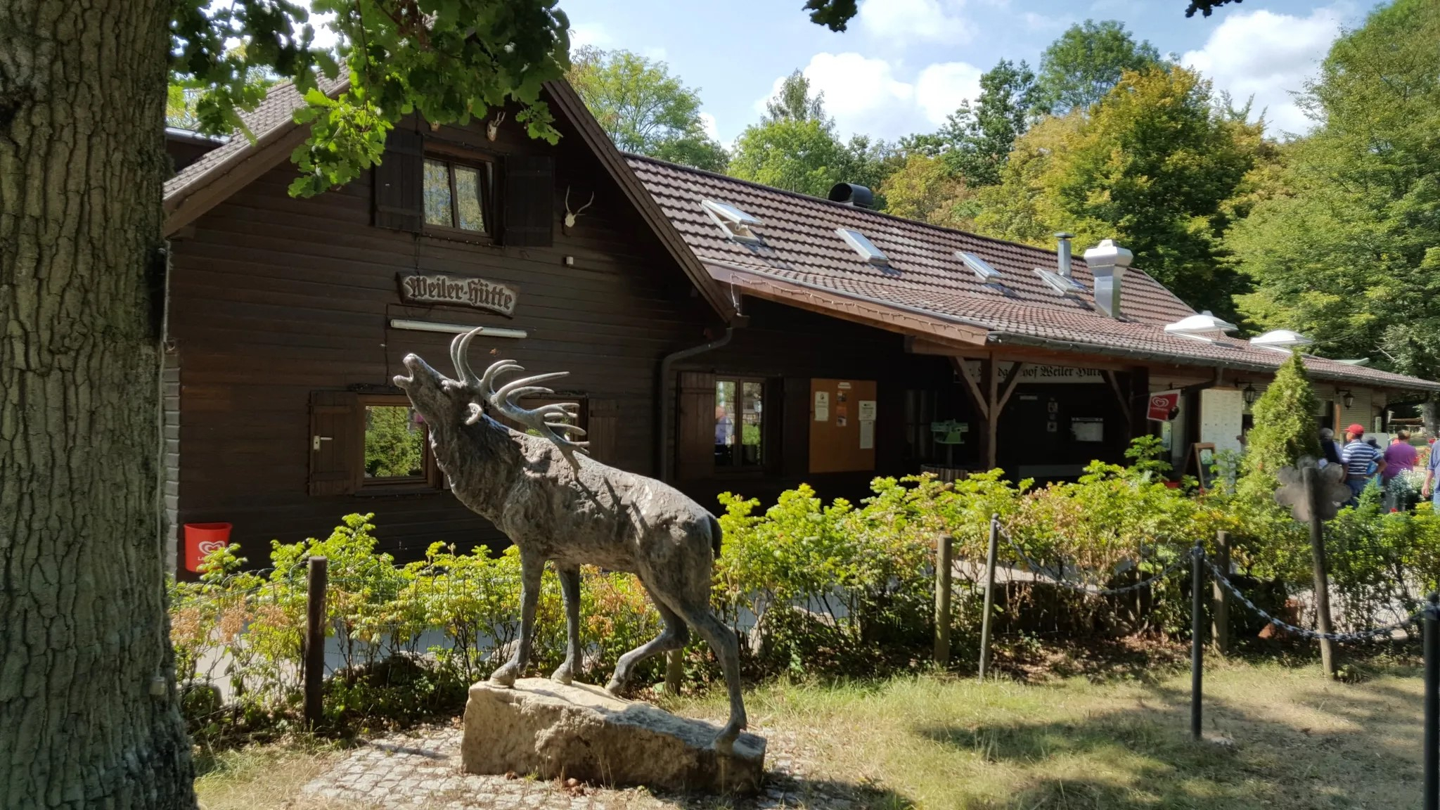 Weiler Hütte im Wald mit Hirschskulptur im Vordergrund